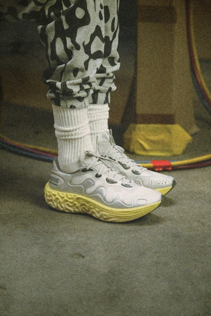 PUMA x Salehe Bembury Velum 2 NITRO in Cool Light Gray worn on foot with slouched white socks on a concrete floor