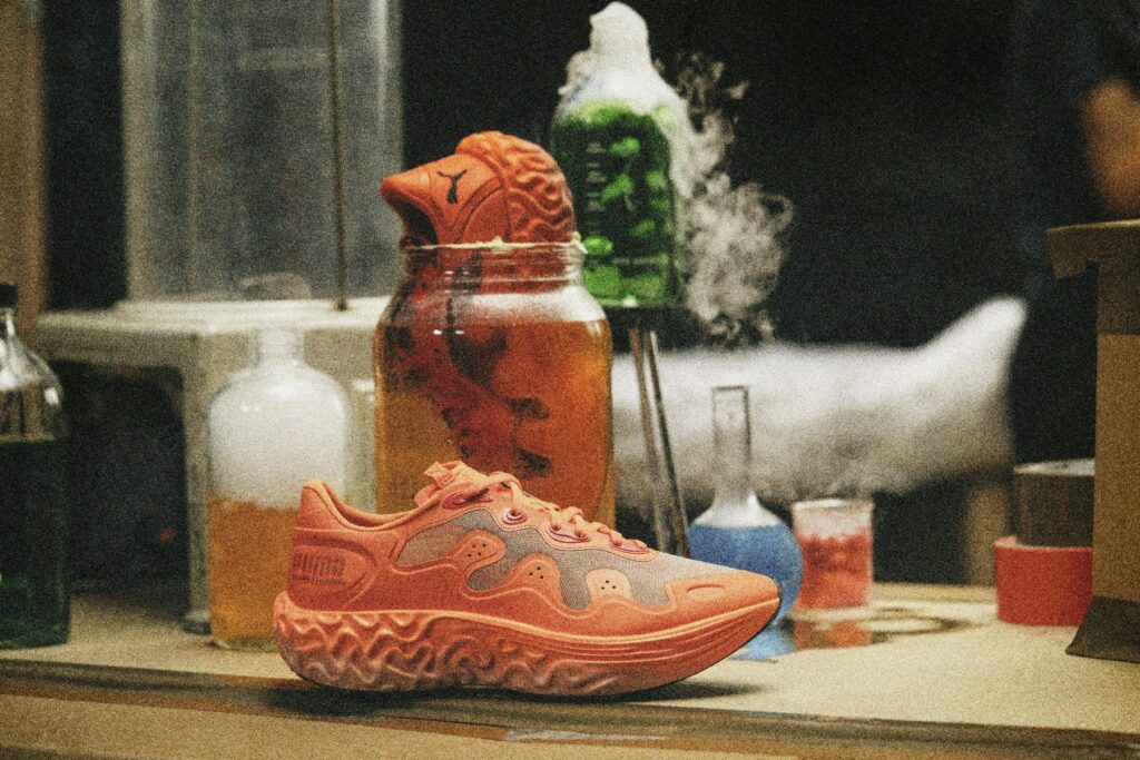 PUMA x Salehe Bembury Velum 2 NITRO in Red Clay-Nasturtium on a laboratory bench surrounded by beakers