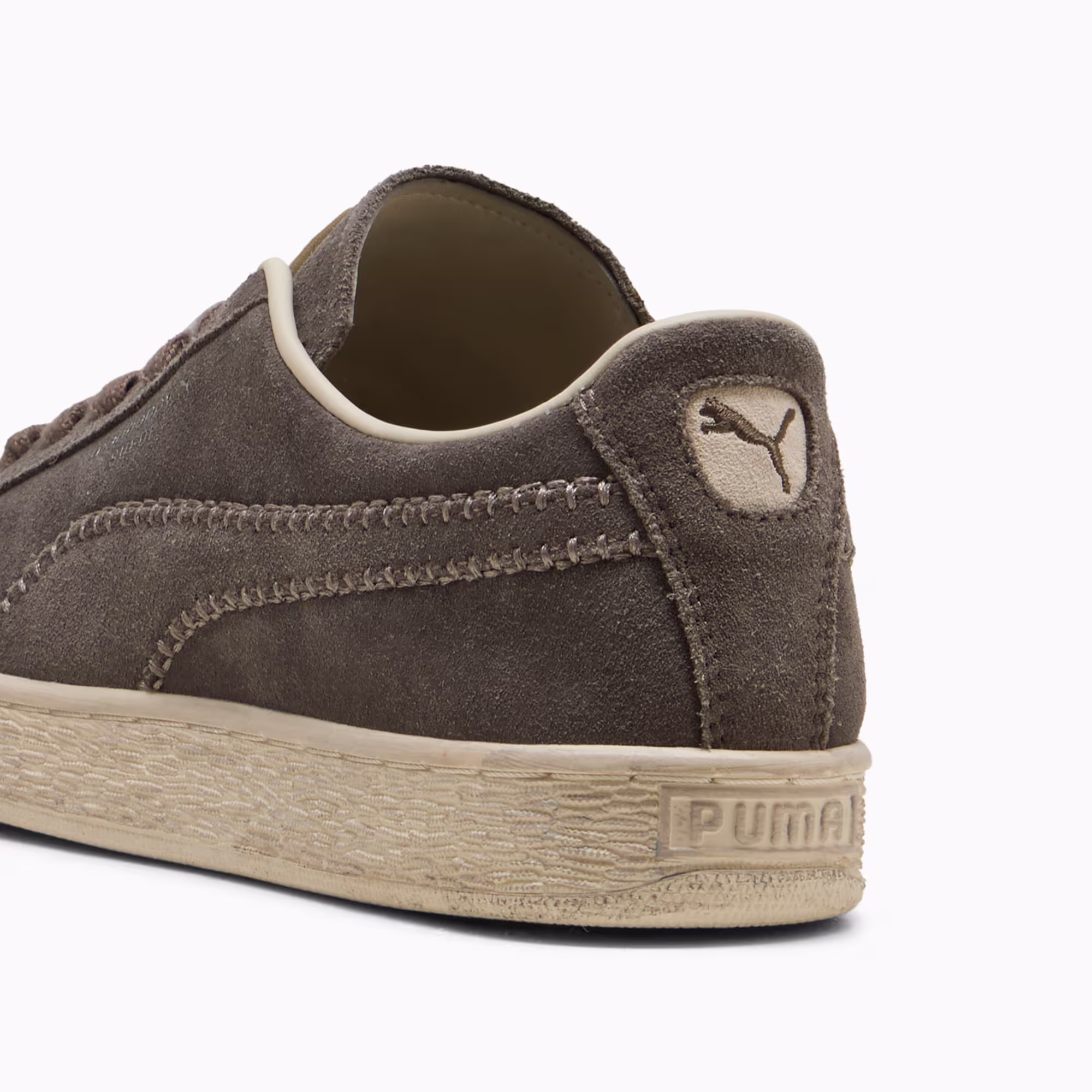 Heel of the PUMA x Madhappy Suede in Matte Bronze and Alpine Snow, showing the whipstitched tonal Formstrip, an embossed PUMA cat on the suede heel and a PUMA wordmark pressed into the raw cream foxing